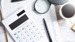 A calculator, pen and magnifier resting on printed financial ledgers